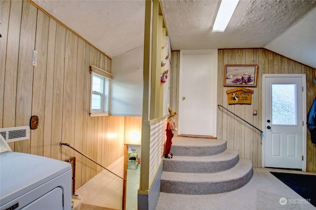 interior space featuring a textured ceiling, washer / clothes dryer, lofted ceiling, and wood walls