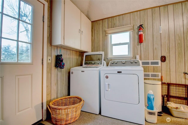 washroom with wood walls, cabinets, separate washer and dryer, and a healthy amount of sunlight