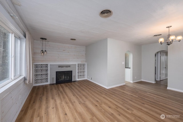 unfurnished living room with a wealth of natural light, a fireplace, hardwood / wood-style floors, and an inviting chandelier