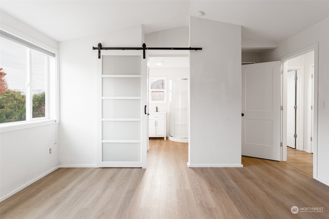 unfurnished bedroom with lofted ceiling, a barn door, light wood-type flooring, and ensuite bath