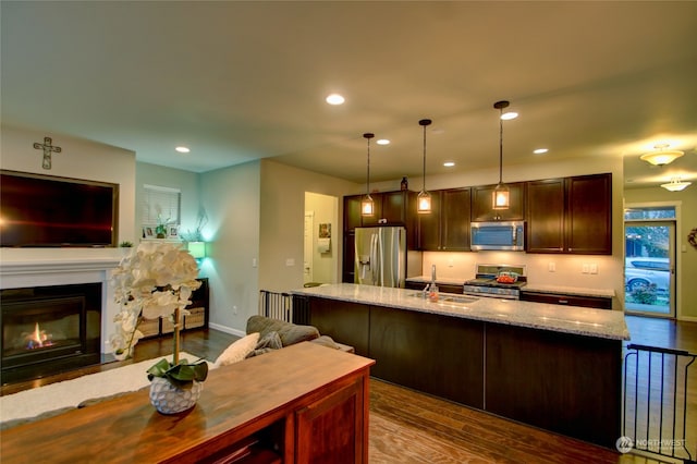 kitchen with sink, hanging light fixtures, dark hardwood / wood-style floors, light stone counters, and stainless steel appliances