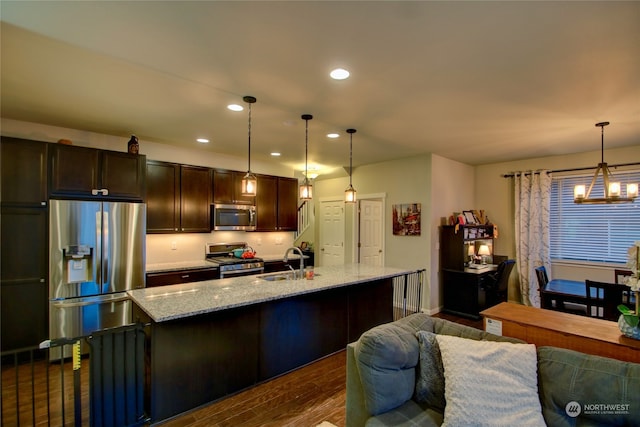 kitchen with a kitchen island with sink, dark wood-type flooring, decorative light fixtures, light stone counters, and stainless steel appliances