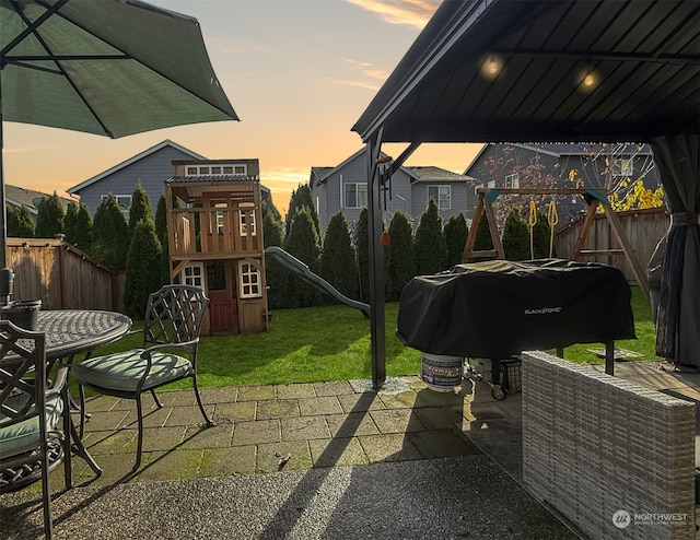 patio terrace at dusk with a lawn, area for grilling, and a playground