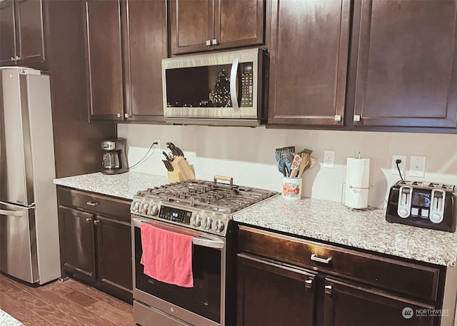 kitchen with dark brown cabinets, light stone countertops, and stainless steel appliances