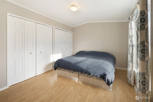 bedroom with two closets, ornamental molding, lofted ceiling, and hardwood / wood-style flooring