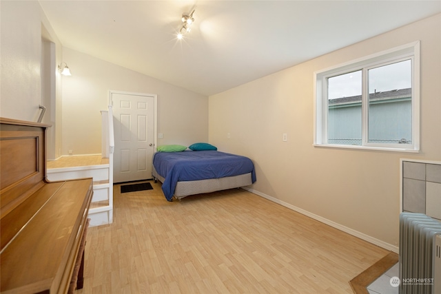 bedroom featuring radiator heating unit, light hardwood / wood-style floors, and lofted ceiling