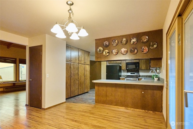 kitchen with hanging light fixtures, kitchen peninsula, a chandelier, black appliances, and light wood-type flooring