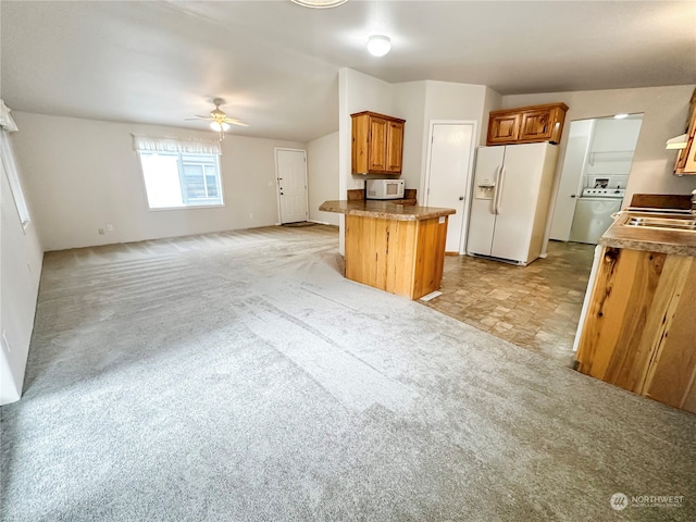 kitchen featuring ceiling fan, kitchen peninsula, white appliances, washer / dryer, and light carpet