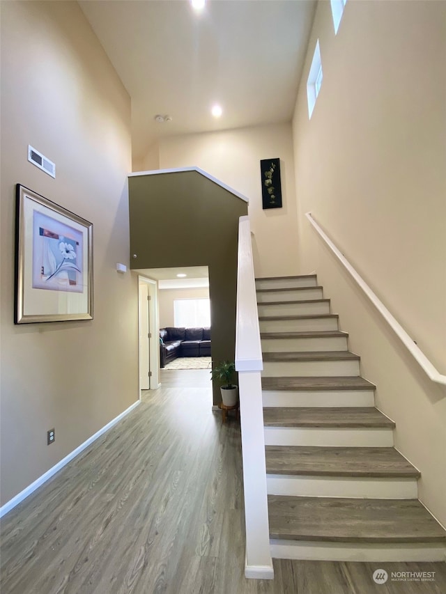 stairs with wood-type flooring and a towering ceiling