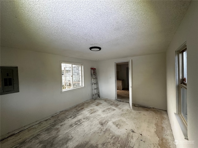 empty room featuring a textured ceiling, electric panel, and light hardwood / wood-style flooring