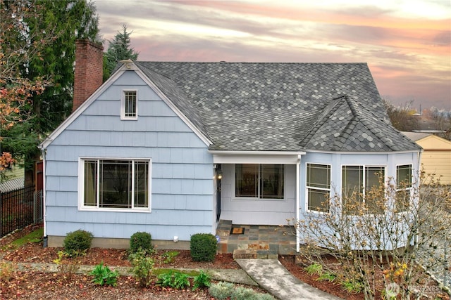 view of front of house featuring a chimney, fence, and roof with shingles