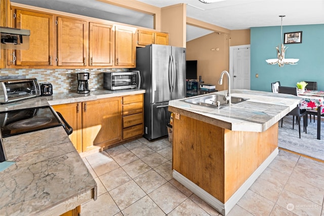 kitchen with tasteful backsplash, vaulted ceiling, sink, decorative light fixtures, and stainless steel refrigerator