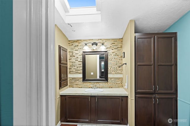 bathroom featuring vanity, a textured ceiling, backsplash, and a skylight