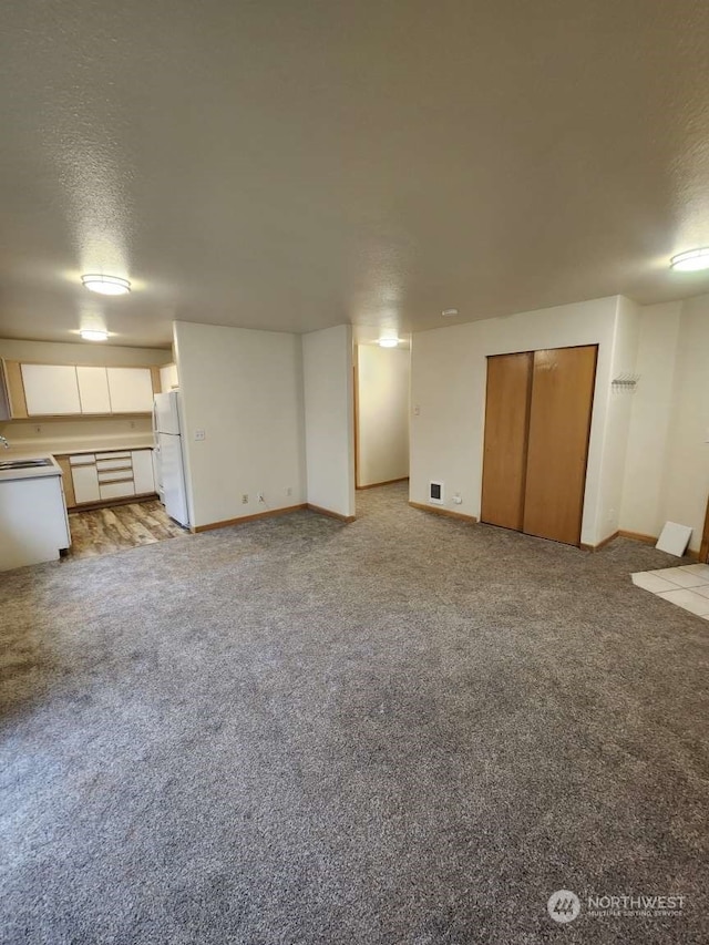 basement featuring light carpet, a textured ceiling, and white fridge