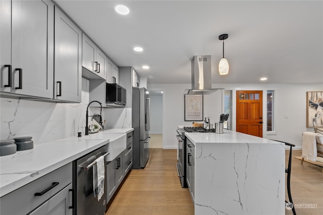 kitchen featuring hanging light fixtures, tasteful backsplash, light hardwood / wood-style flooring, island range hood, and appliances with stainless steel finishes