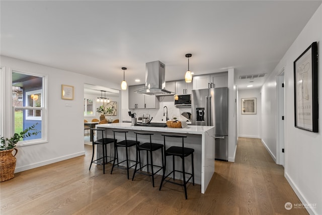 kitchen with gray cabinetry, high end refrigerator, light hardwood / wood-style floors, decorative light fixtures, and island range hood