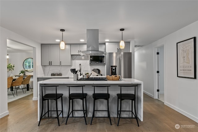 kitchen with stainless steel appliances, gray cabinets, island range hood, a breakfast bar, and light wood-type flooring