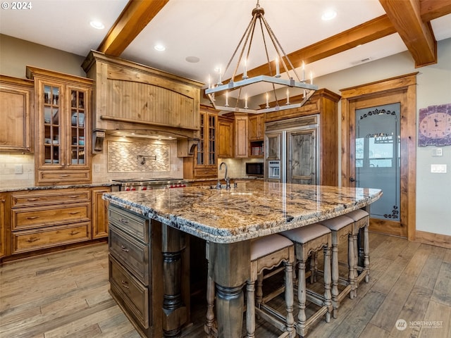 kitchen featuring decorative backsplash, appliances with stainless steel finishes, a kitchen island with sink, pendant lighting, and wood-type flooring