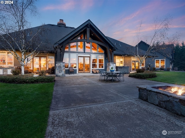 back house at dusk featuring french doors, a patio area, and a lawn