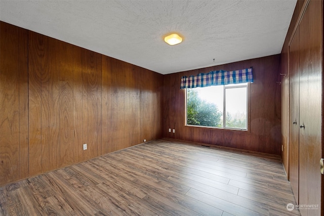 spare room featuring wood walls, a textured ceiling, and light wood-type flooring