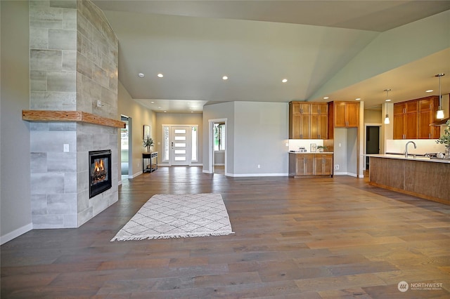 unfurnished living room featuring sink, dark wood-type flooring, high vaulted ceiling, and a tiled fireplace