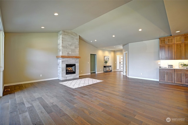 unfurnished living room with hardwood / wood-style floors, vaulted ceiling, and a tiled fireplace