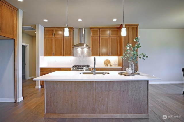 kitchen featuring wall chimney exhaust hood, a kitchen island with sink, sink, pendant lighting, and dark hardwood / wood-style floors