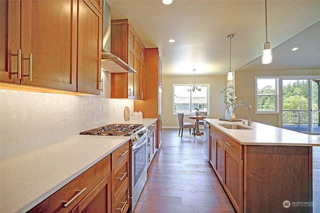 kitchen featuring sink, stainless steel appliances, wall chimney range hood, wood-type flooring, and a kitchen island with sink