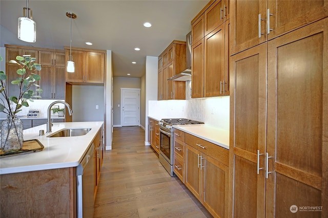 kitchen featuring sink, hanging light fixtures, wall chimney range hood, light hardwood / wood-style floors, and appliances with stainless steel finishes