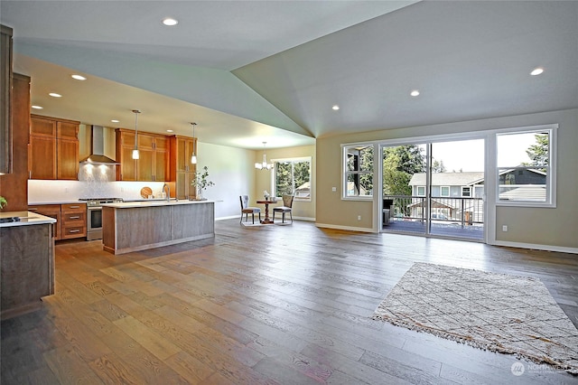 kitchen with stainless steel gas range oven, hanging light fixtures, vaulted ceiling, hardwood / wood-style flooring, and wall chimney exhaust hood