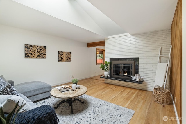 living room with hardwood / wood-style flooring, a brick fireplace, and lofted ceiling