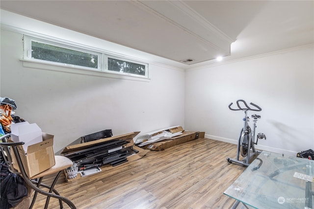 exercise room featuring crown molding and light wood-type flooring