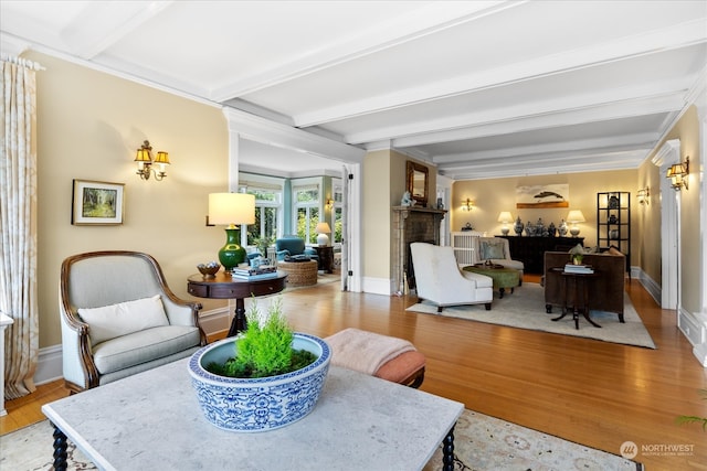 living room featuring a brick fireplace, crown molding, beamed ceiling, and light wood-type flooring