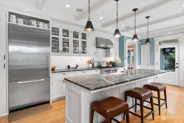 kitchen featuring white cabinets, wall chimney exhaust hood, light hardwood / wood-style floors, beam ceiling, and stainless steel appliances