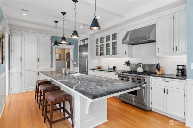 kitchen with high end range, light wood-type flooring, a kitchen island with sink, and range hood