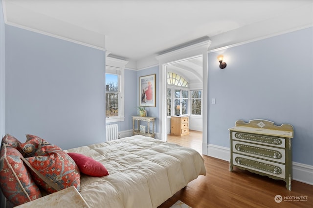 bedroom with wood-type flooring, radiator heating unit, and crown molding