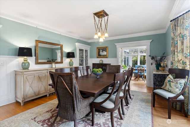 dining space with light wood-type flooring, ornamental molding, and an inviting chandelier