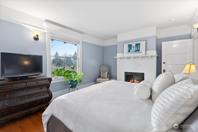 bedroom with wood-type flooring, a brick fireplace, and crown molding