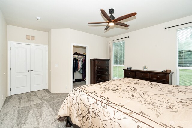 bedroom with a walk in closet, ceiling fan, and light carpet