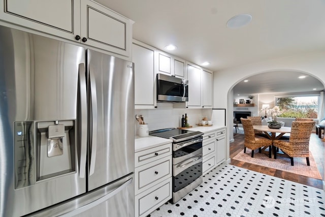 kitchen with backsplash, white cabinets, stainless steel appliances, and light hardwood / wood-style floors