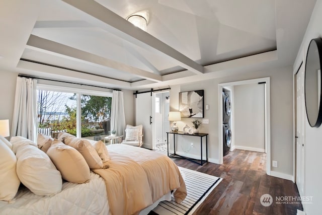 bedroom featuring a spacious closet, a barn door, dark hardwood / wood-style flooring, vaulted ceiling, and stacked washer / drying machine