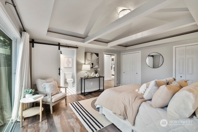 bedroom featuring hardwood / wood-style floors, a barn door, ensuite bathroom, and multiple closets