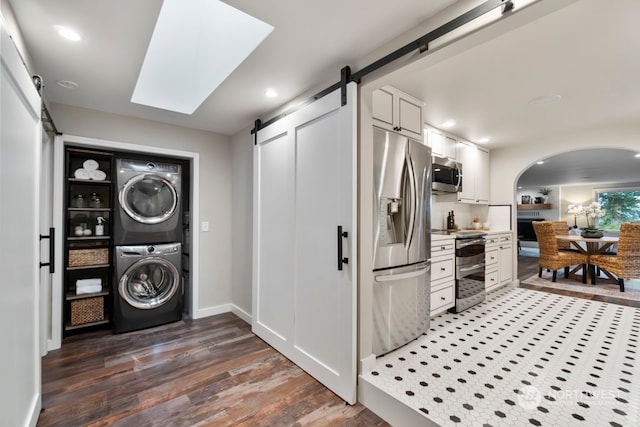 laundry area with dark hardwood / wood-style floors, a barn door, stacked washer and dryer, and a skylight