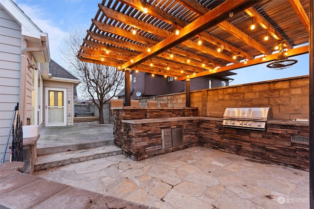 patio terrace at dusk featuring an outdoor kitchen, grilling area, and a pergola