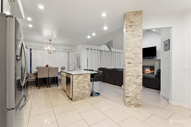 kitchen with a kitchen breakfast bar, stainless steel appliances, light tile patterned floors, a center island with sink, and hanging light fixtures