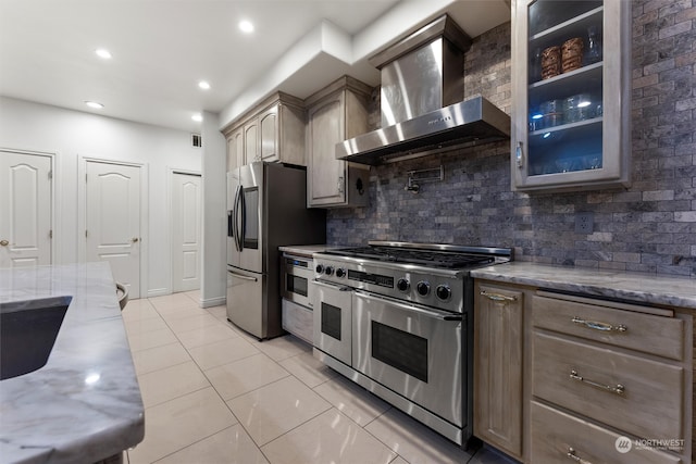 kitchen with wall chimney exhaust hood, light stone countertops, decorative backsplash, and stainless steel appliances