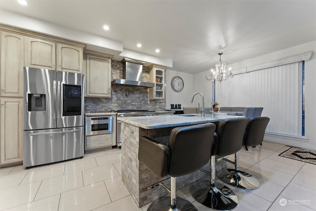 kitchen featuring sink, wall chimney exhaust hood, decorative backsplash, a center island with sink, and appliances with stainless steel finishes