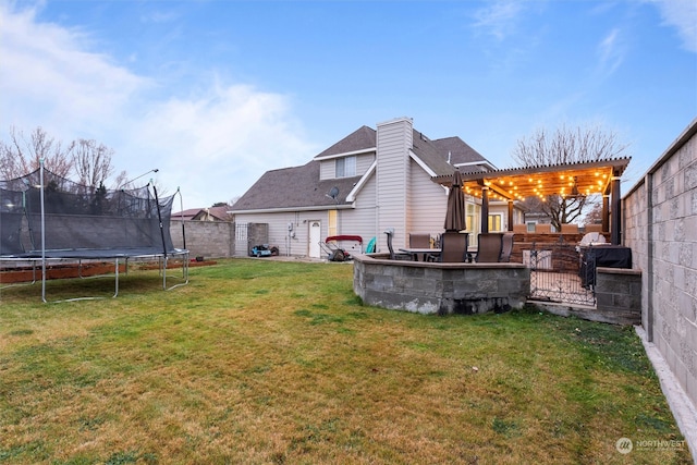 rear view of property with a lawn, a trampoline, and a pergola