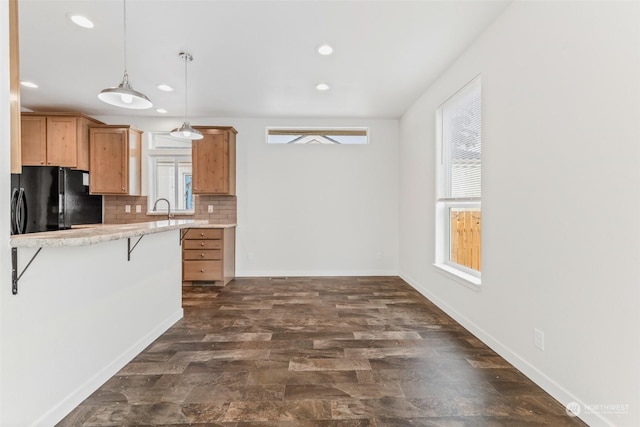 kitchen featuring pendant lighting, backsplash, black fridge, sink, and a kitchen bar