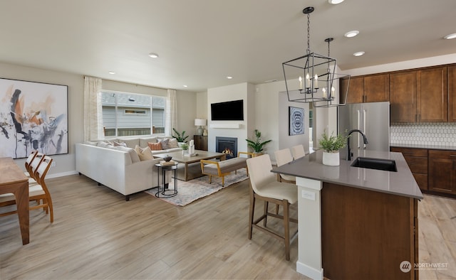 kitchen with a center island with sink, sink, decorative backsplash, light hardwood / wood-style floors, and stainless steel refrigerator